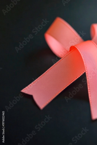 A pink ribbon lying on a table, possibly as a symbol or decoration. vertical frame