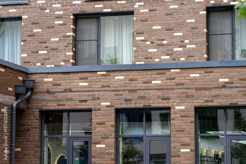 Close-up of modern brick building facade featuring striking pattern of brown and lighter bricks, large dark-framed windows, and corner with drainage system, highlighting contemporary urban architectur