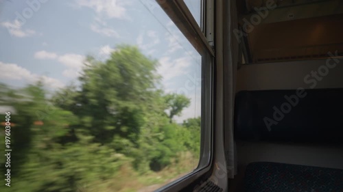 Beautiful countryside scenery rushing by as seen from the window of a moving train. The view shows a blur of green trees under a cloudy sky