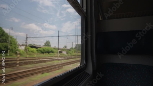 Point of view shot from a moving train showing the landscape with railroad tracks, power lines, and trees passing by under a cloudy sky