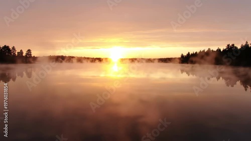 Watching a serene sunrise over a misty lake with calm water and silhouetted trees