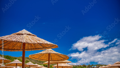 Fotografija Tropical beach with straw umbrellas and golden sand under a clea