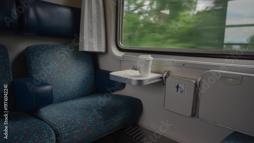 Interior of a comfortable train with an empty seat next to the window. A fresh coffee cup is on the table as the countryside passes by