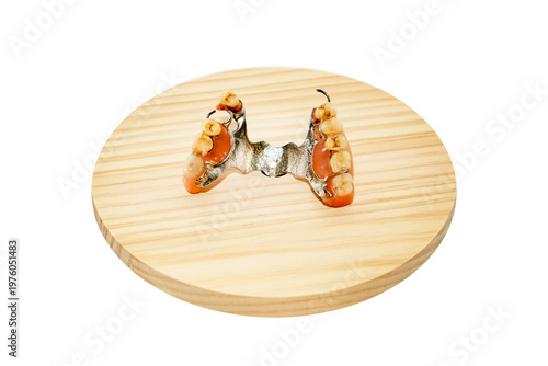 Removable partial denture with artificial teeth and metal base placed on round wooden platform isolated on white background. Studio product photography. Dentistry and dental prosthetics concept.