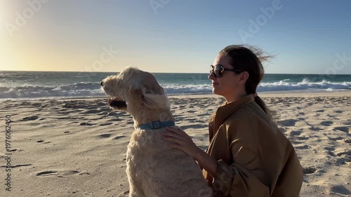 A woman enjoys a walk with her dog along the beach while waves crash in the background