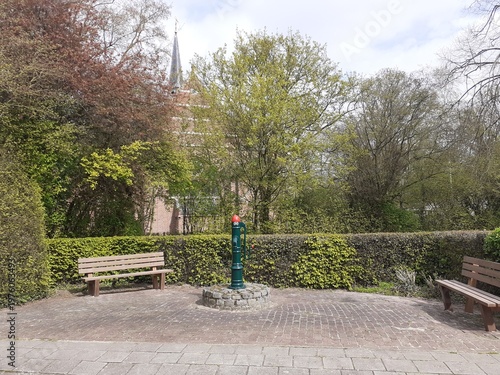 an old parish pump at a square with two benches in a little village 'Hengstdijk' in the dutch countryside in springtime