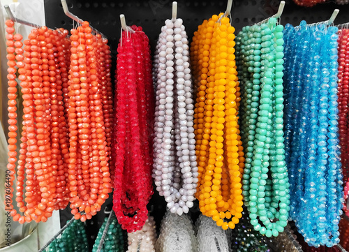 Colorful strands of beads hanging on display, variety of vibrant glass beads for jewelry making, craft supplies in different colors, textured background with rich assortment