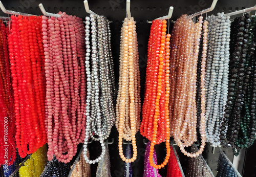 Colorful strands of beads hanging on display, variety of vibrant glass beads for jewelry making, craft supplies in different colors, textured background with rich assortment
