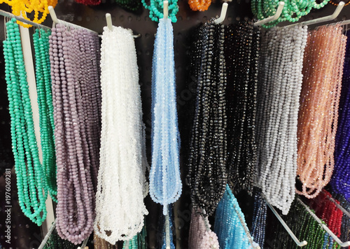 Colorful strands of beads hanging on display, variety of vibrant glass beads for jewelry making, craft supplies in different colors, textured background with rich assortment