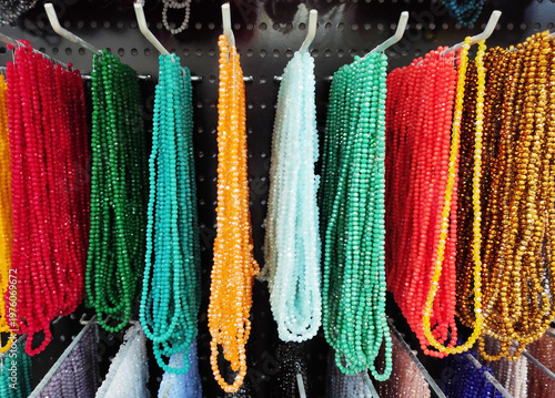 Colorful strands of beads hanging on display, variety of vibrant glass beads for jewelry making, craft supplies in different colors, textured background with rich assortment
