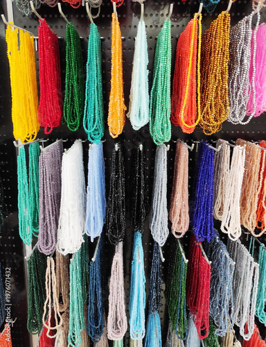 Colorful strands of beads hanging on display, variety of vibrant glass beads for jewelry making, craft supplies in different colors, textured background with rich assortment