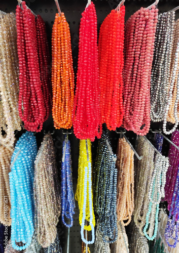 Colorful strands of beads hanging on display, variety of vibrant glass beads for jewelry making, craft supplies in different colors, textured background with rich assortment