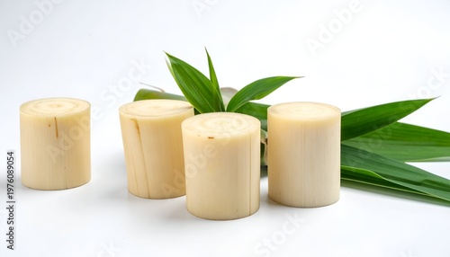 Close-up studio shot featuring four cylindrical, pale plant sections, possibly palm hearts, with fresh green leaves. White background