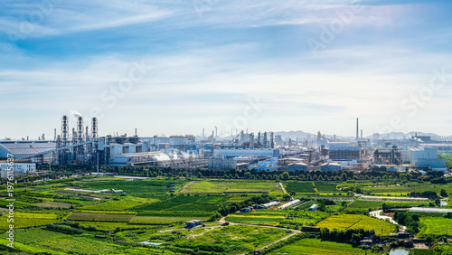 Extensive industrial park and chemical manufacturing facilities located next to vibrant green agricultural fields under a clear blue sky.