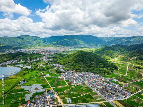 Aerial view of a picturesque rural village surrounded by lush green mountains and agricultural fields.