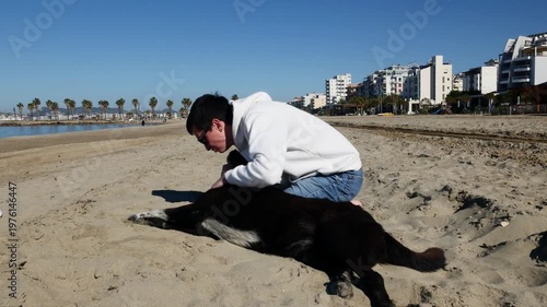 Smiling young man gently petting stray dog on the beach.