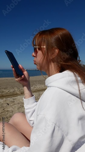 Young woman using AI voice chat on smartphone by the sea.