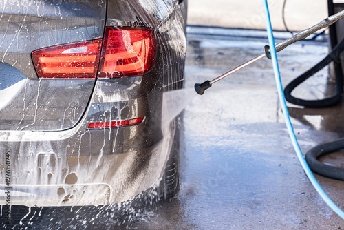car being cleaned with high-pressure water jet at a self service car wash. White foam, wet metal texture and splashing water 