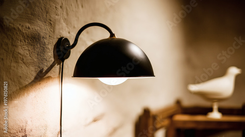 interior scene featuring a sleek matte black wall sconce mounted on a textured gray plaster wall. The fixture emits soft warm light both upward and downward, creating a gentle halo glow that 