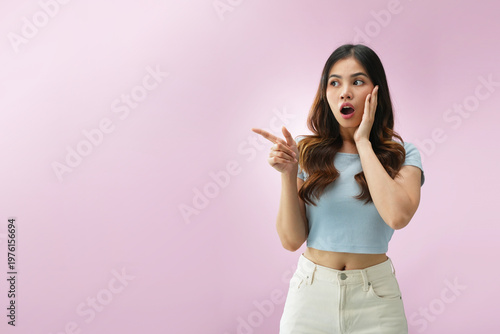 Obraz na plátně Indonesian woman pointing to the side with open-mouth curious expression, reacti
