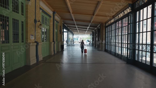 Alone woman with her luggage walking down a long, elegant corridor of a historic train station, symbolizing travel, departure, and solitude