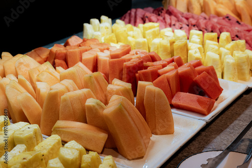 An attractive display of freshly sliced fruits including melons, pineapples, and papayas, artfully arranged to highlight their vibrant colors and inviting textures.