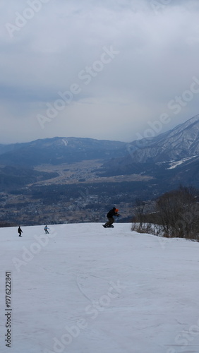 Snowboarder jumps over snowy slope with distant village and mountain landscape