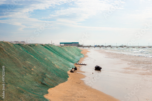 Billede på lærred Green netting used to combat erosion and oil spills on a sandy beach against a backdrop of waves