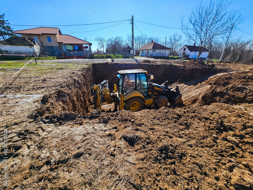 Foto Backhoe loader excavating large foundation pit at rural construction site
