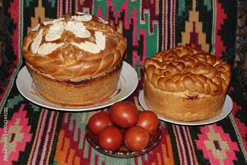 Traditional Easter bread on a colorful geometric kilim rug. Golden braided bread decorated with almonds and red Easter eggs. Festive folk style, warm tones, vibrant colors, appetizing still life.