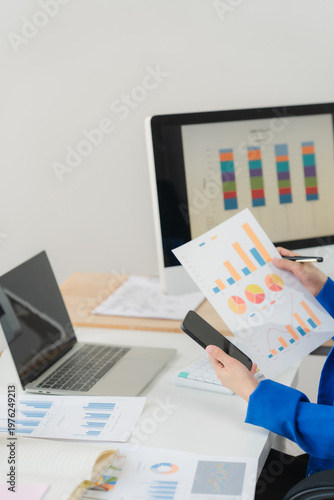 Young Asian businesswoman focused confident reviewing financial document chart graph report analyzing data paperwork desk modern office workplace corporate analytical accounting planner