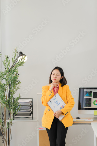 Thoughtful Businesswoman in Modern Office: A focused businesswoman, clad in a vibrant yellow blazer, ponders complex decisions within a contemporary office setting.