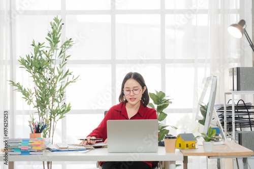 Focused Professional: A focused individual intently works at her desk with a laptop, the scene bathed in natural light and set within a modern, organized office space.