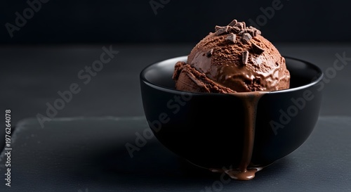Rich dark chocolate ice cream scoop melting in black bowl.