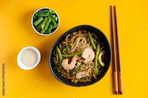 Stir fry noodles with shrimps and green beans in bowl on yellow background