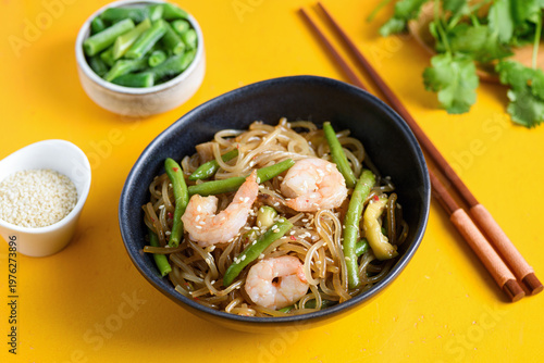 Stir fry noodles with shrimps and green beans in bowl on yellow background