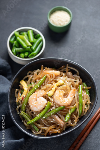 Asian stir fry glass noodles with shrimps and green beans in bowl, black background
