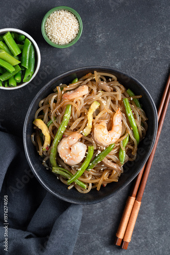 Asian stir fry glass noodles with shrimps and green beans in bowl, black background