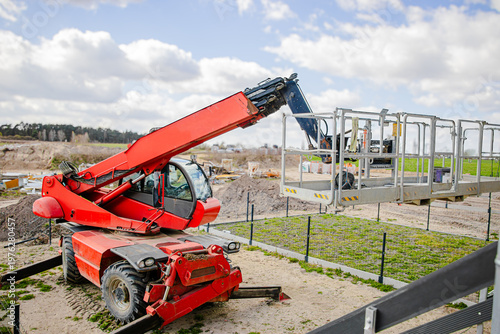 Tableau sur toile Red telescopic handler lifting a platform above green crops on a construction si
