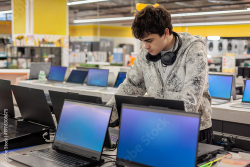 Fotografía Teenage boy comparing laptops in an electronics store and choosing a device