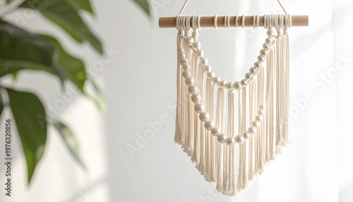 Creamy macrame wall hanging with beaded accents, wood dowel, near a plant