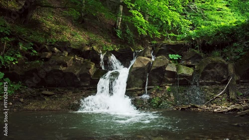 Beautiful mountain waterfall and magical green forest at sunny summer day. Crystal clear water. Calm natural wonder, quiet place for green tourism concept