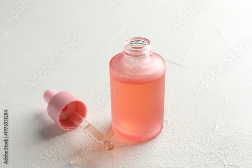 Bottle of cosmetic product and pipette on light textured table, closeup