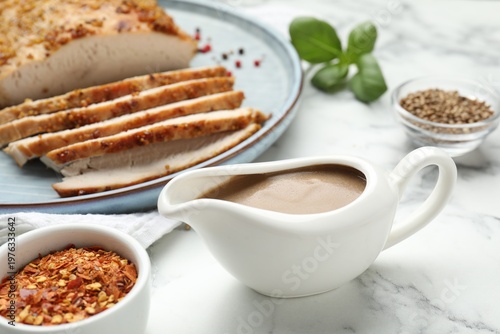 Photos Turkey gravy in sauce boat, baked meat and spices on white marble table, closeup