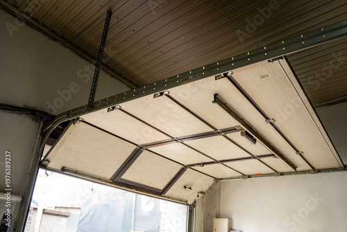 Fotografie Interior view of an open sectional garage door with metal tracks and ceiling panels, showing workshop entrance and overhead mechanism