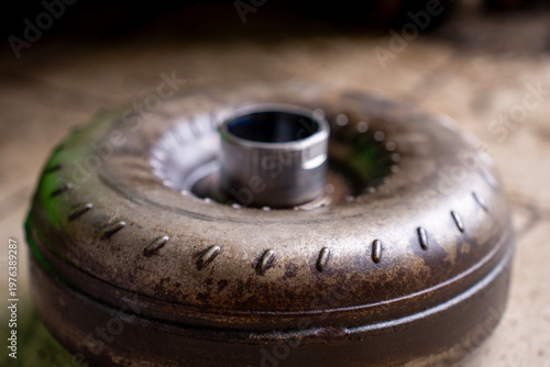 Fotografie Top view of a used torque converter from an automatic transmission placed on a workshop floor, showing metal housing and central hub