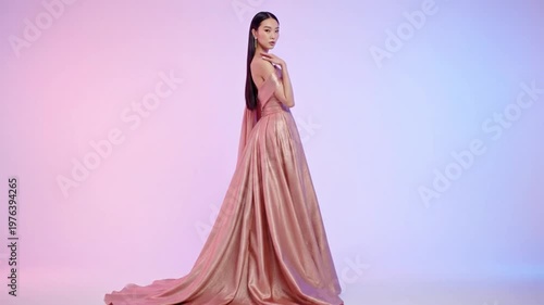 Elegant Asian woman gracefully poses in a stunning off-the-shoulder shimmering rose gold evening gown with a dramatic train.