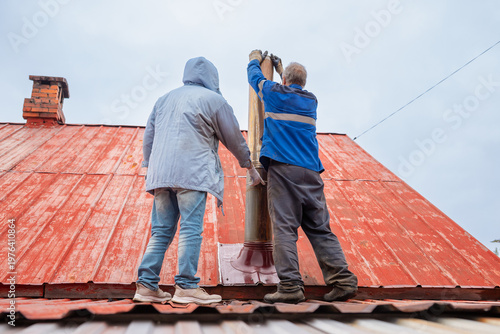 Canvastavla Two men chimney sweepers repairing metal chimney pipe on house roof
