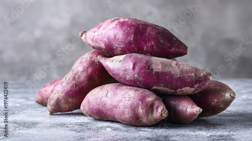 A pile of whole unpeeled ube purple yams on a textured grey background, showcasing the natural dusty skin and vibrant purple hue of the tubers.