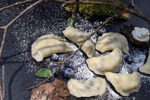 Photos Sweet berry dumplings sprinkled with flour on a black slate decorated with mossy forest branches